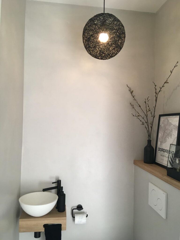 Exclusieve badkamerrenovatie met beton ciré in Amstelveen Sfeervolle zwarte design hanglamp boven een modern fonteintje in een betonlook toiletruimte in Amstelveen